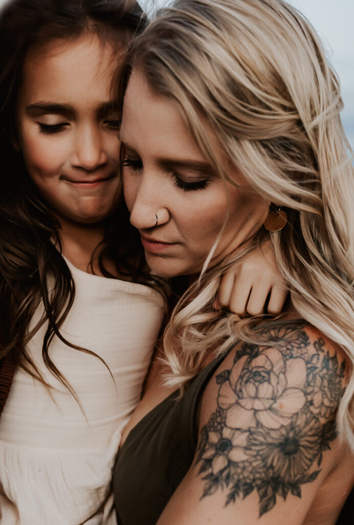Family Photographer, a young mother holds her daughter close. Mom has a floral tattoo on her arm.