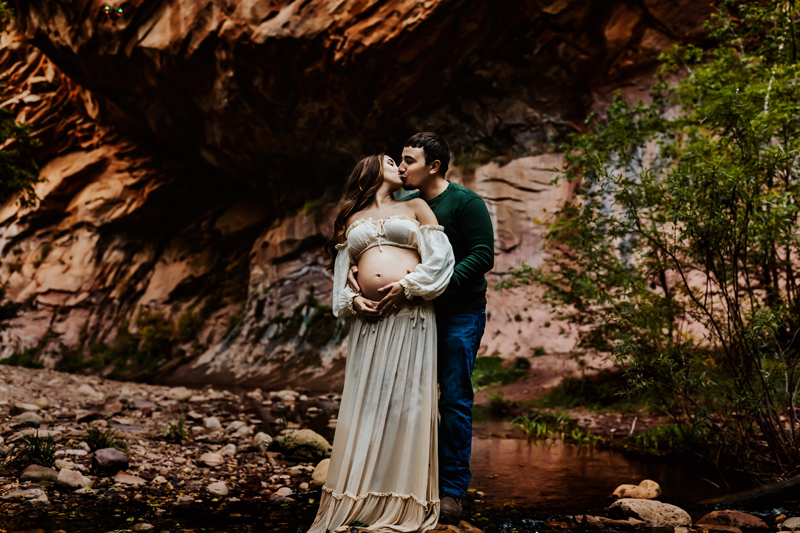 Maternity Photographer, a husband and wife embrace, she is pregnant. They stand outside in nature.