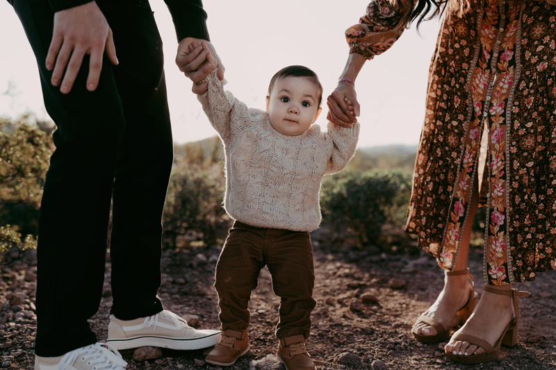 Family Photographer, a mother and father hold their young son's hands as he walks